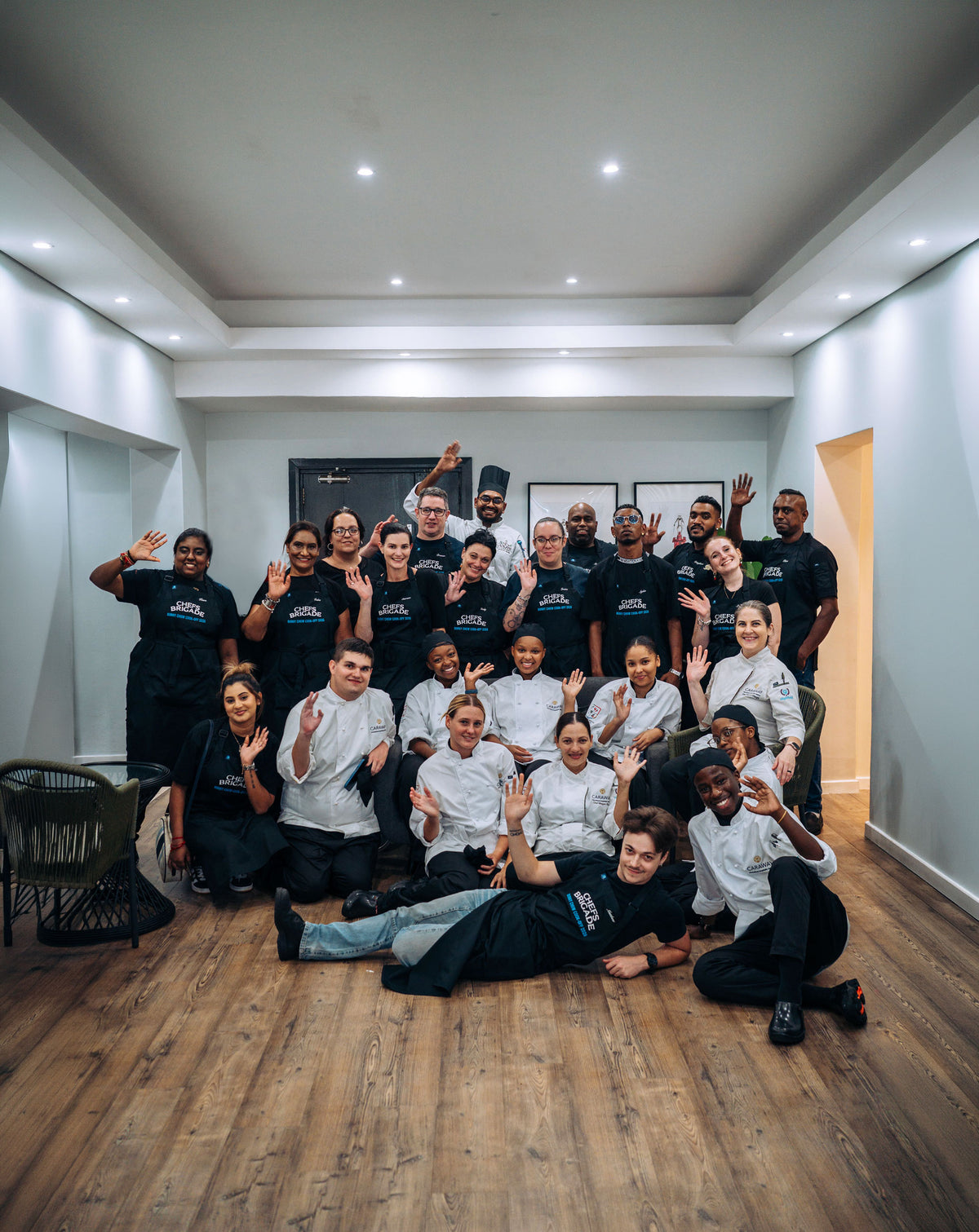 Group of people in black and white uniforms posing together in a room with wooden flooring and white walls.