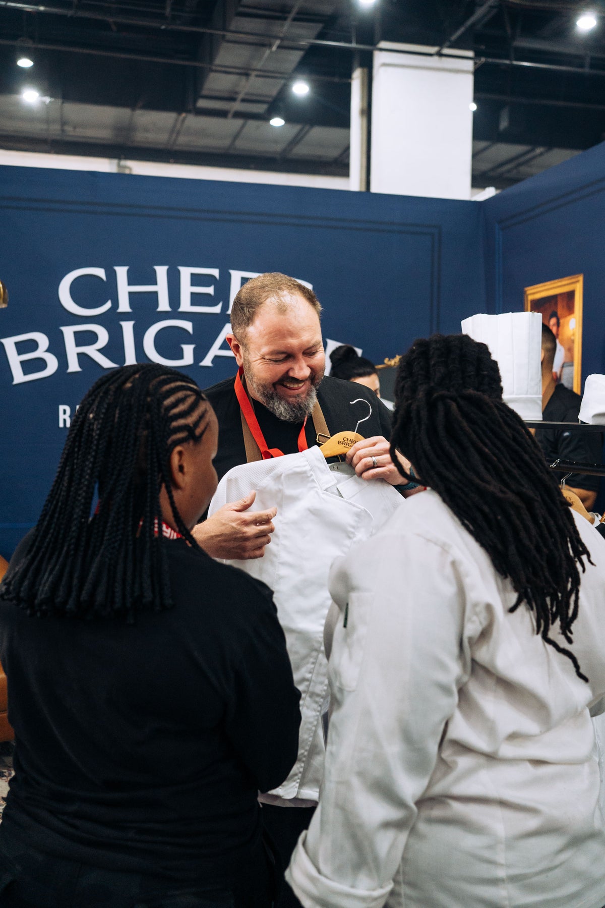 Man interacting with two people in front of a 'Chiefs Brigade' sign.