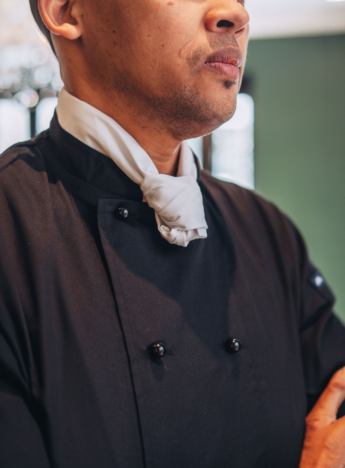 Person wearing a black chef's coat with a white necktie.